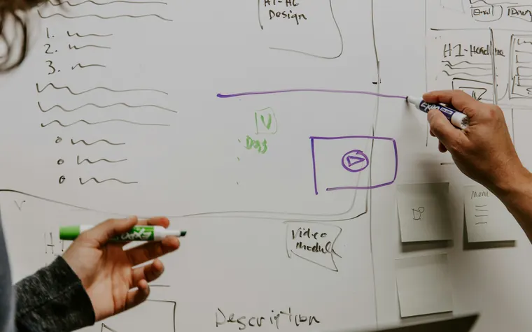 Manos dibujando un diagrama de pantallas en una pizarra blanca